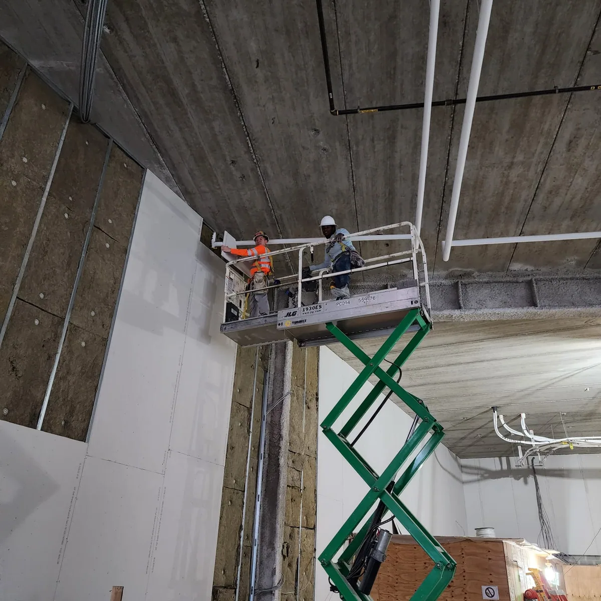 Drywall crew installing tall wall board using approved access equipment available at the project
