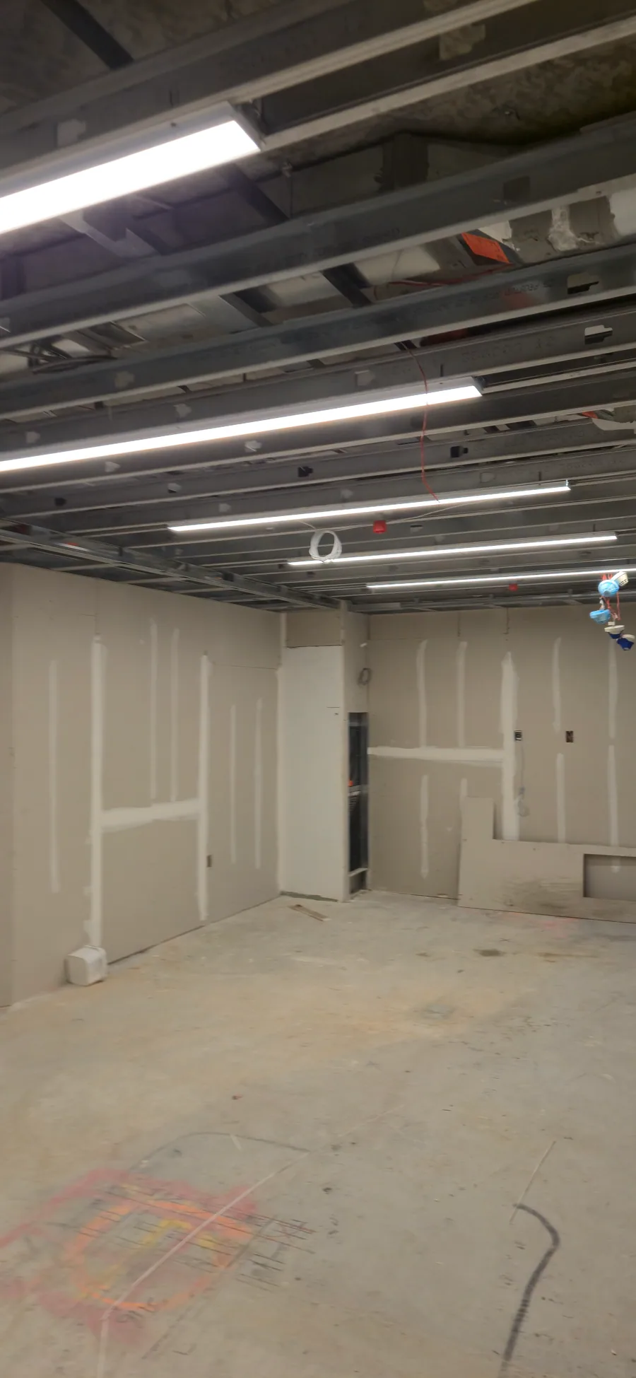 Interior room with drywall board installed around walls and ceiling framing