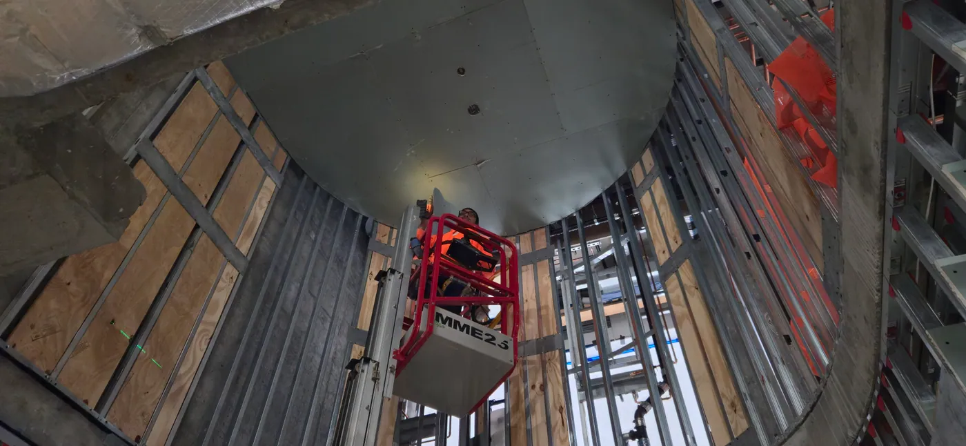 Worker installing ceiling drywall board using approved access equipment available inside commercial framing